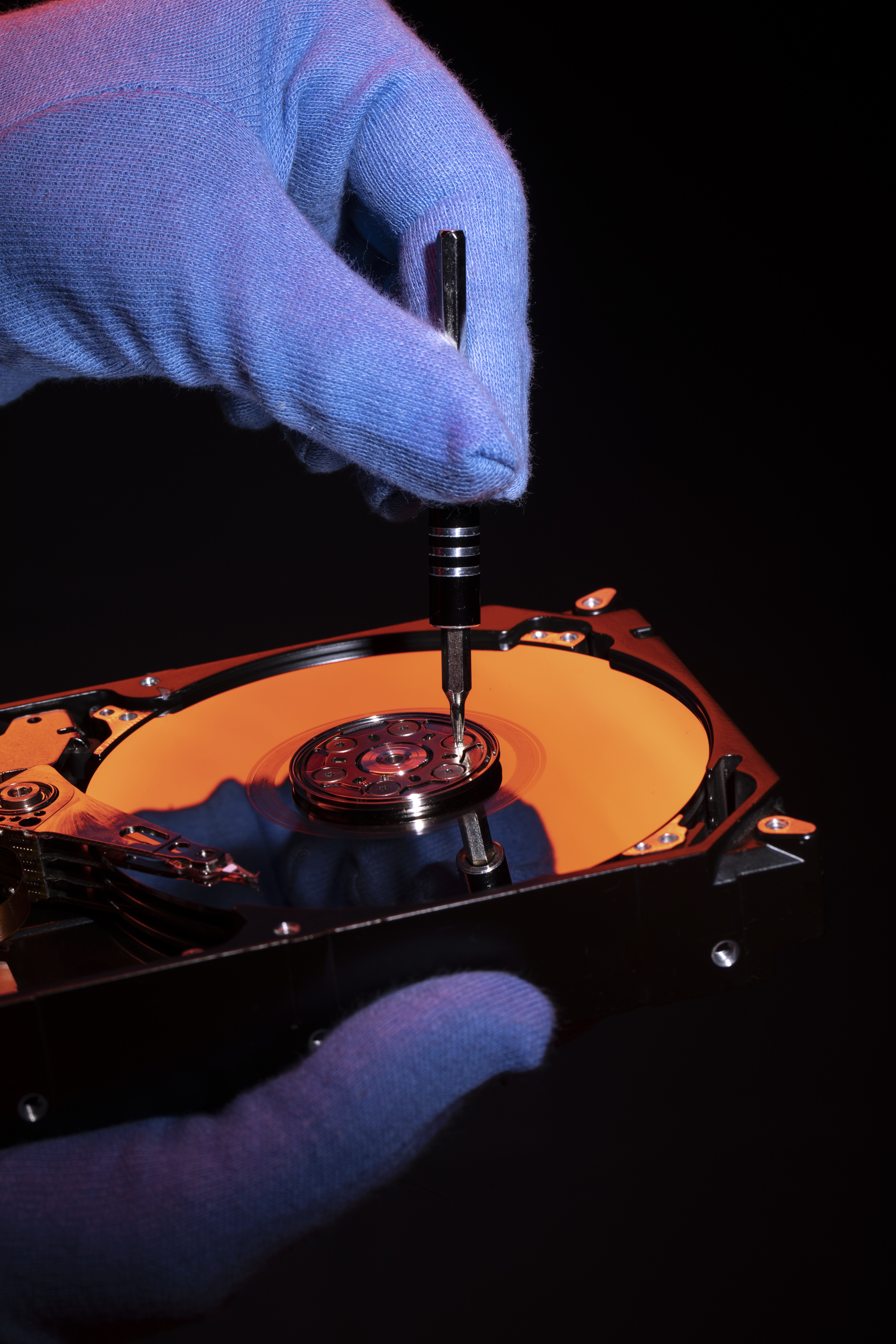 Image main d'une personne avec un gant réparant un disque d'ordinateur sur un fond orange